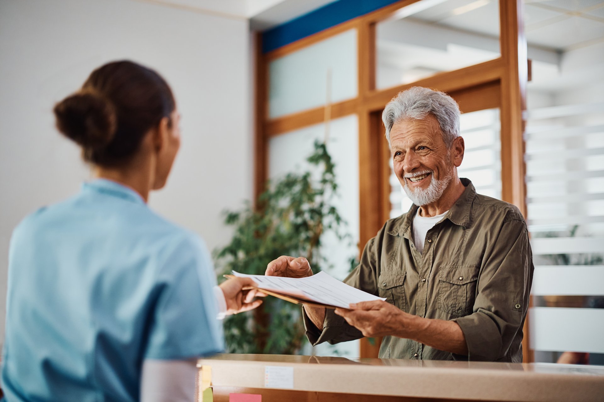 Happy senior man receiving his medical documents from nurse at reception desk at doctor's office